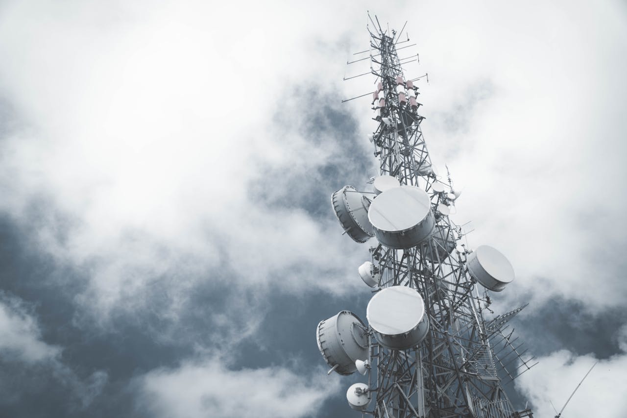 A towering communication mast with satellite dishes, set against a cloudy sky.